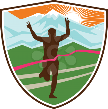 Retro style illustration of a silhouette of victorious marathon runner flashing victory hand sign with snow capped mountains and sunburst and finish line ribbon tape in shield or crest shape.