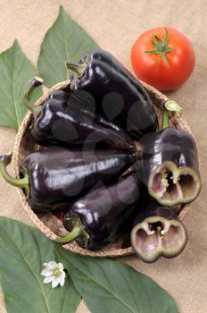 Royalty Free Photo of Black Peppers in a Basket With One Tomato and Leaves Around It