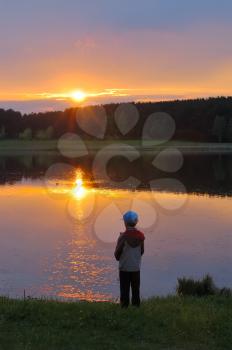 Royalty Free Photo of a Boy at the Shore of a Lake at Sunset