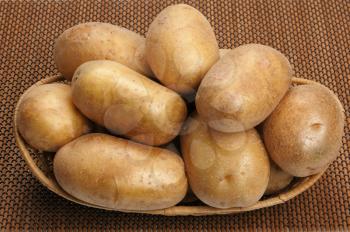Several brown potatoes in a basket on a mat