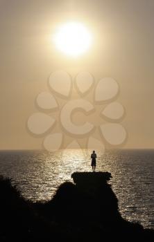 A young man stands on the remains of the Crusader wall above the sea at sunset