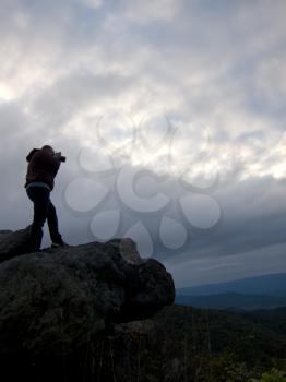Royalty Free Photo of a Person Taking Pictures on the Top of a Mountain at Dusk With an Overcast Sky