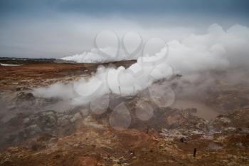 Desolate landscape of Iceland volcanic brown soil with steamy geyser mist and grey colored sky