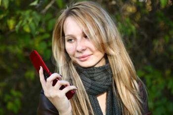 Young cute girl with long blond hairs with cell phone. Fall. Autumn. Outdoor session.