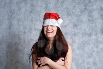 Attractive 20-25 years brunette smiling topless woman in Santa hat studio on grey.