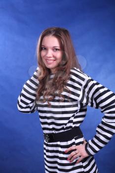 Young brunette lady in stripped dress posing on grey background