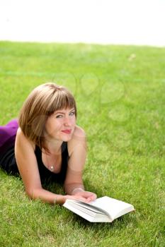 beautiful young female student reading a book outdoors laying on grass