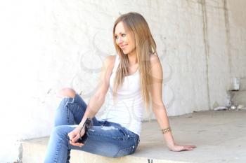 Outdoor photo of pretty girl sitting on the floor in grungy setting.