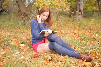 redhead young woman outdoors in the field reading in autumn park