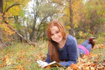 Young beautiful girl with red hair reading a book outdoor in autumn park