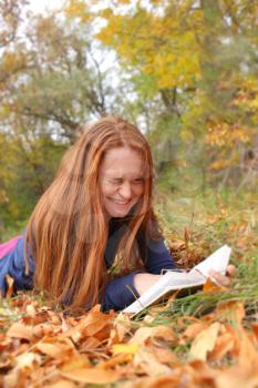 Redhead woman lies on green grass and reads book. Happy smiling beautiful young university student studying lying down in grass.