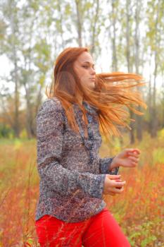 Beautiful young redhead in a autumn meadow wind blowing