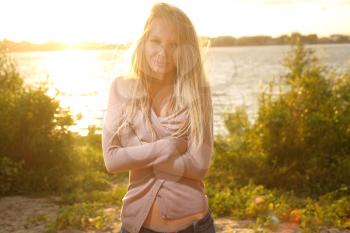 blond girl near river against sun on sunset