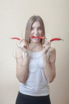 Pretty blond woman head and shoulders shot holding in hands red spicy pepper and biting another one on beige background. Healthy nutrition diet concept