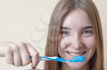 Closeup of young woman with a tooth brush on her hands about to brush her teeth on beige background