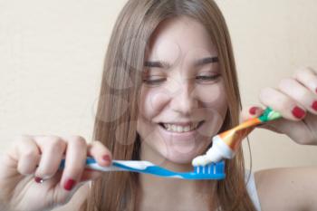 Closeup of young woman with a tooth brush on her hands about to brush her teeth on beige background