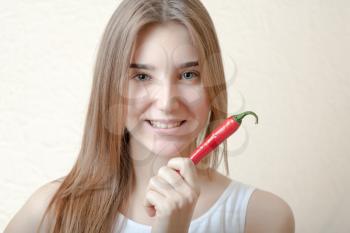 pretty blond woman head and shoulders shot holding in hands red spicy pepper on bege background. Healthy nutrition diet concept