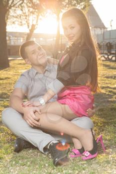 Romantic young couple relaxing outdoors in park on grass in backlit smiling