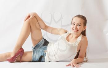 sexy blond woman in white shirt and jeans shorts lying (laying) on a floor on white background
