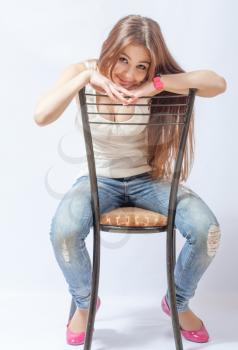 A young blond woman resting on a chair in a white blouse and blue jeans for white background in the studio.