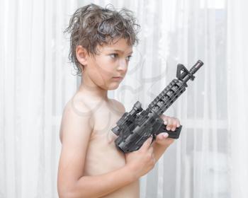 Portrait of little boy with automatic weapon on white background indoors