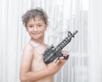 Portrait of little boy with automatic weapon M16 on white background indoors