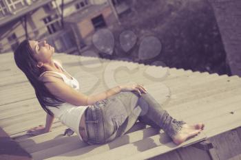 brunette women sit on the roof of the building, vintage toned image, summertime freedom concept
