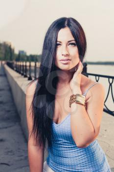 cute long haired brunette 20s girl weared blue tank top outdoors sitting and posing in fashion style on riverside. Toned cross process color image