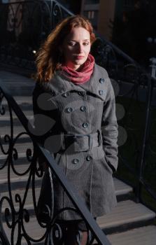 redhead 20s women outdoor in autumn park, weared scarf and coat, standing on the stairs