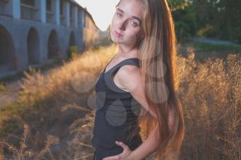 mysterious looking image of 20s young female with long blond hair posing against sunset golden light in park. Backlit shot.