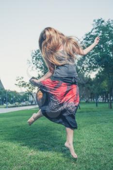 The long haired 20s women jumps on a green grass in evening time in city park . Girl jumping like flying bird.