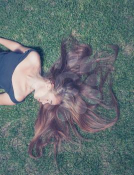 Crossprocess color image of the beautiful young girl is lying on green grass in the evening time. She enjoy summertime