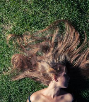 beautiful young girl is lying on green grass in the evening time. The girl lays on a grass of a meadow