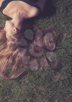 Toned image of the beautiful young girl is lying on green grass in the evening time.