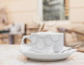horizontal shot, cup of fresh cappuchino on the table, interior of cafe on background