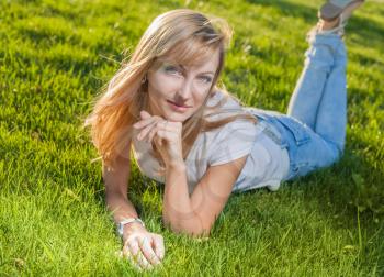 blonde women lay on grass and looking at camera, diagonal composition