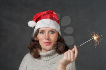 mrs Santa with blank expression studio shot. Cute girl in Santa hat holding sparklers