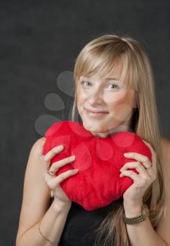 Vertical shot of the beautiful young woman holding a heart shaped red pillow and smiling