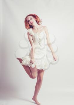 Young woman in white dress, jumps up. On gray background.