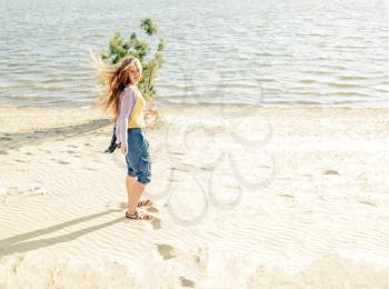 Wind in hair. Beautiful girl standing  in the morning on the beach.