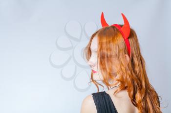 close up of a red haired girl with horns like a devil looking away of camera