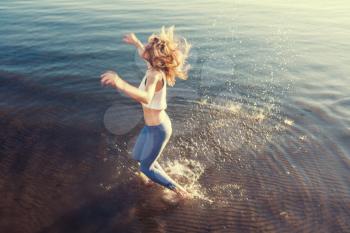 outdoor portrait of young beautiful blonde woman jumping in waves