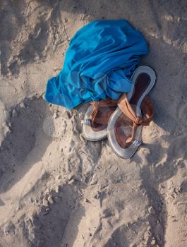 Flip-flops and blue fabric laying over a sand near sea