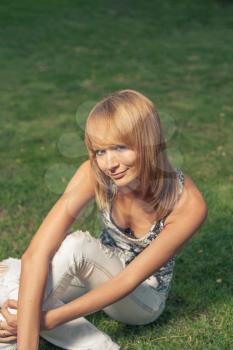 Blond haired girl relaxing sitting on summer grass