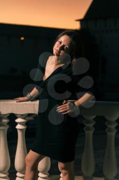 Brunette in small black dress posing near a banister