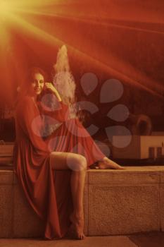 Retro looking photo of women in red dress sitting near fountain.