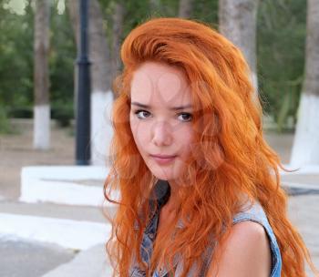 Head and shoulders image of a young women with red hair outdoors.