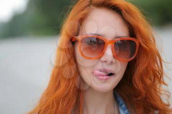 Young red haired women posing in trendy orange sunglasses with her tongue out
