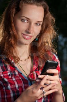 Carrot-top women (redhead) communicate via cell phone. Cute women looking at camera and smiling with mobile phone in her hands.