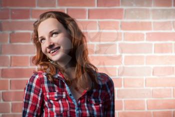 Ginger haired girl posing outdoors against red brick wall and looking away, a lot of copy-space